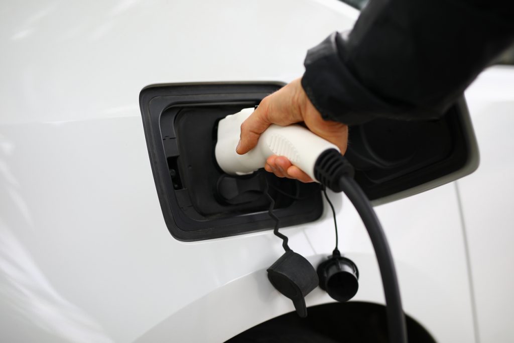 Driver inserts electric charger into vehicle. Charging stations for electric vehicles concept
