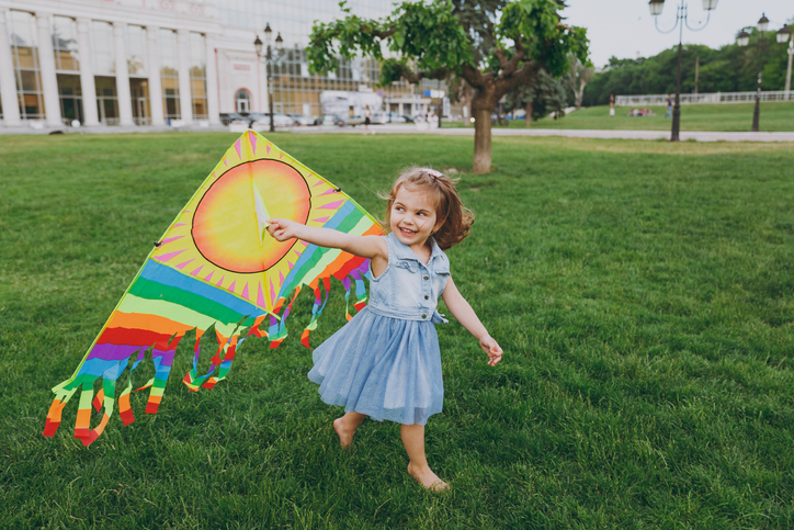 Joyful little cute child baby girl in denim dress walking, play with colorful kite and have fun in green park. Mother, little kid daughter. Mother's Day, love family, parenthood, childhood concept